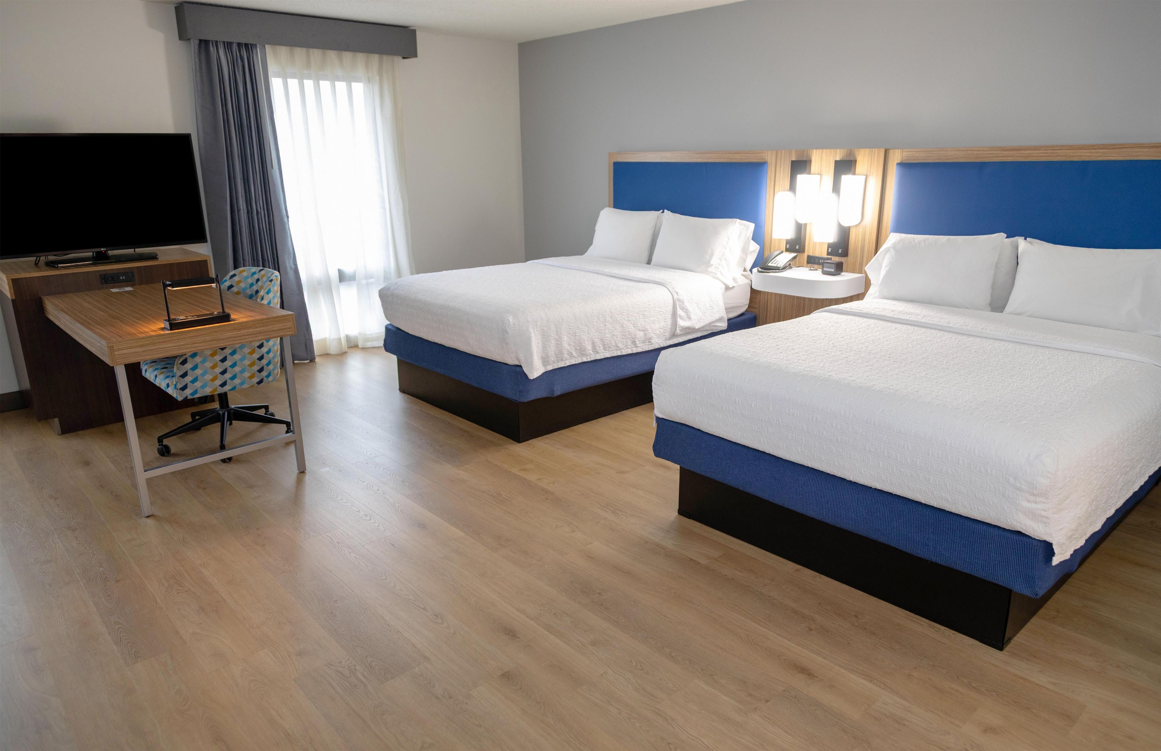 Une chambre d’hôtel avec deux lits, un bureau avec une télévision et une fenêtre avec des rideaux.