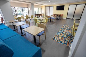 A modern indoor space with tables, chairs, and a blue sofa. - Hampton Inn Madison Huntsville Airport (Madison)