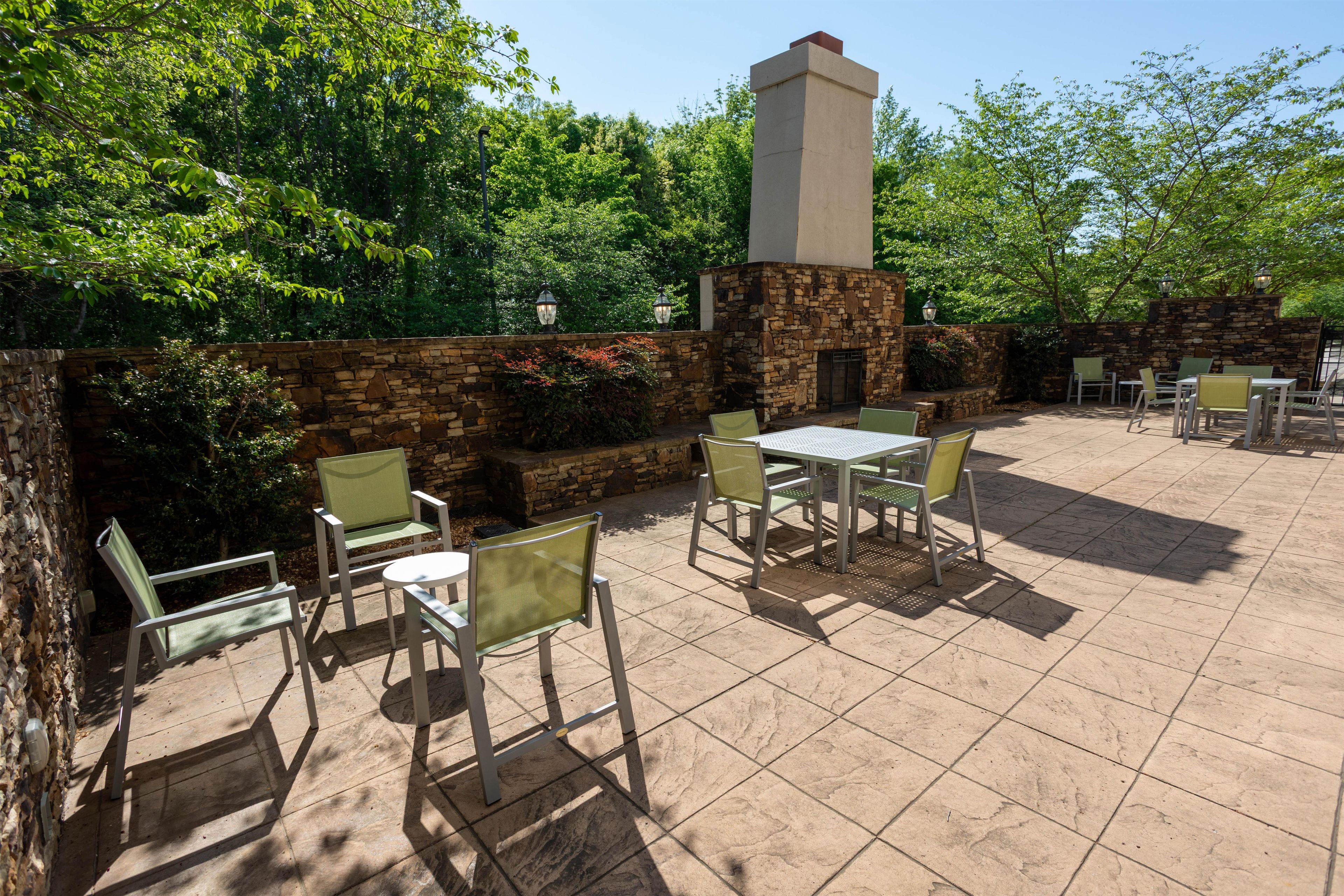 Un patio al aire libre con paredes de piedra, sillas y mesas verdes.