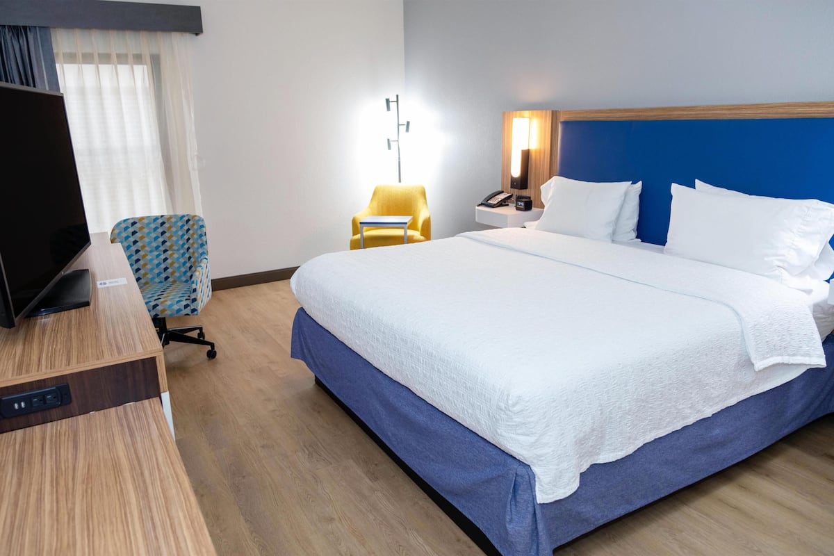 A hotel room with a bed, a TV, a desk, a chair, a nightstand, and a lamp.
