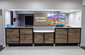 A reception desk with a 'Welcome to Hampton' sign, a cityscape artwork, and a Hilton sign. - Hampton Inn Madison Huntsville Airport (Madison)