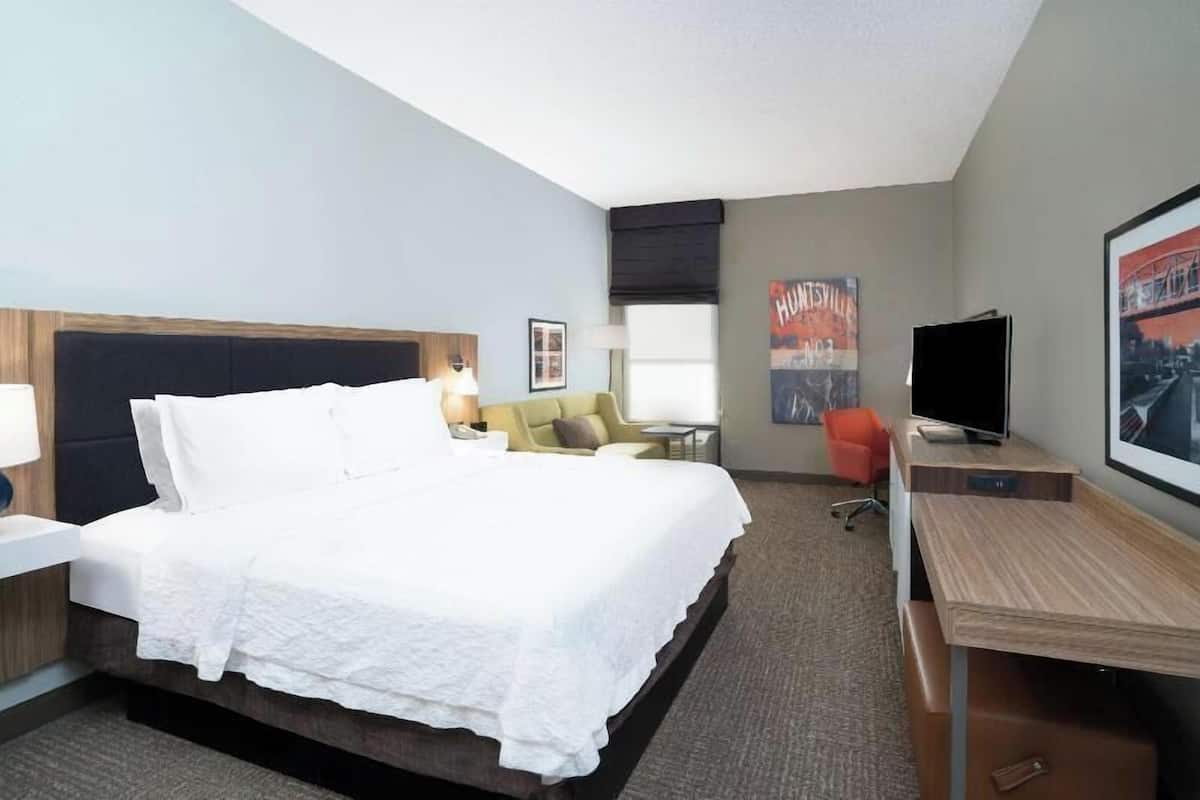 A hotel room with a bed, a desk, a chair, a TV, and a painting on the wall.