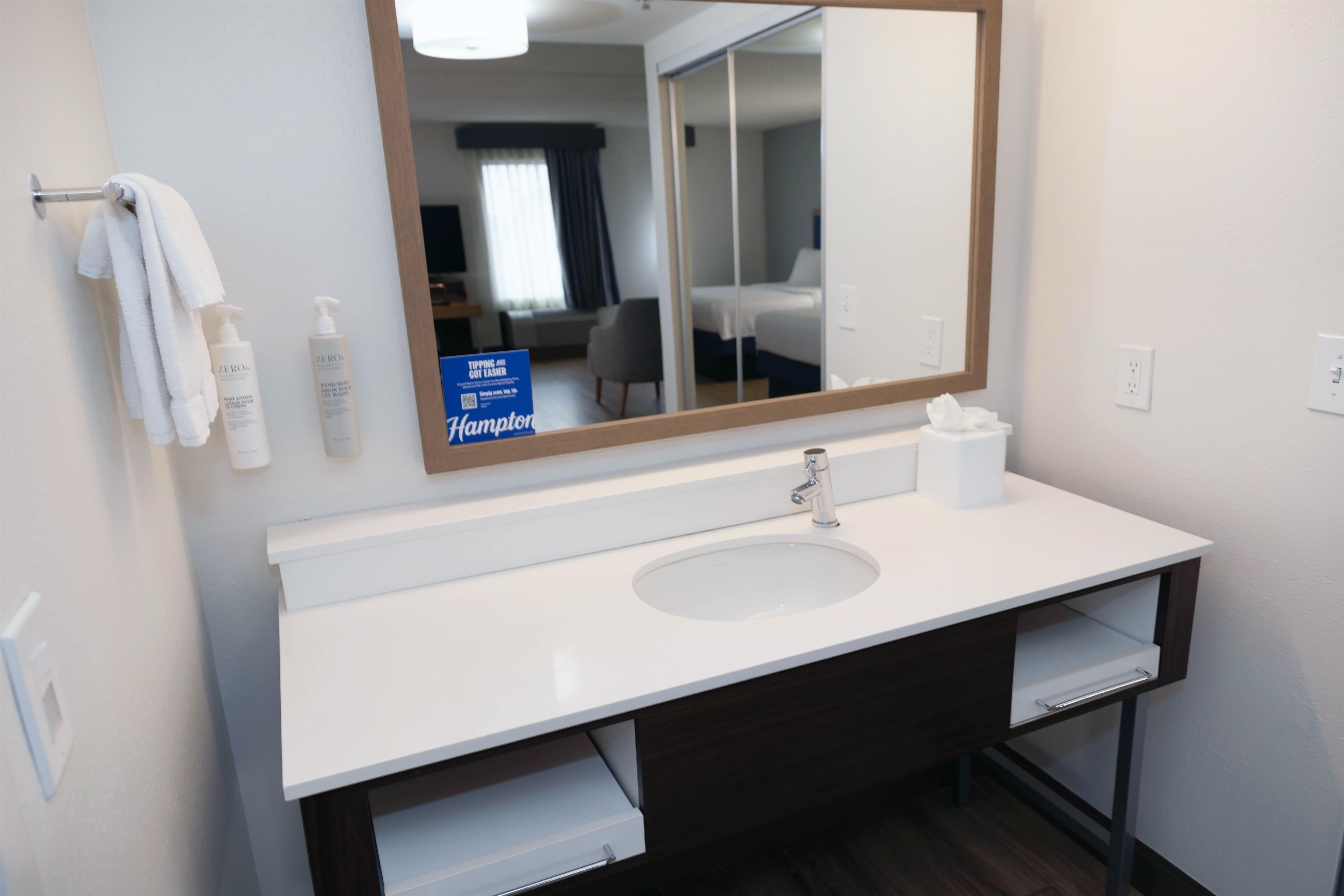 A hotel bathroom with a white sink, a large mirror, and toiletries on the wall.