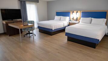 A hotel room with two beds, a desk, a TV, and a window with curtains.