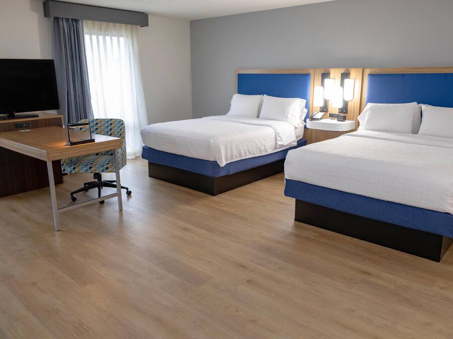 A hotel room with two beds, a desk, a TV, and a window with curtains.