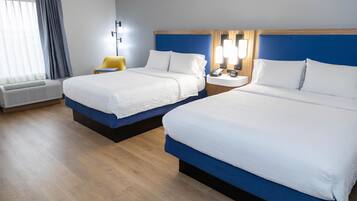 A hotel room with two beds, a bedside table with a lamp, a chair, and a window with curtains.