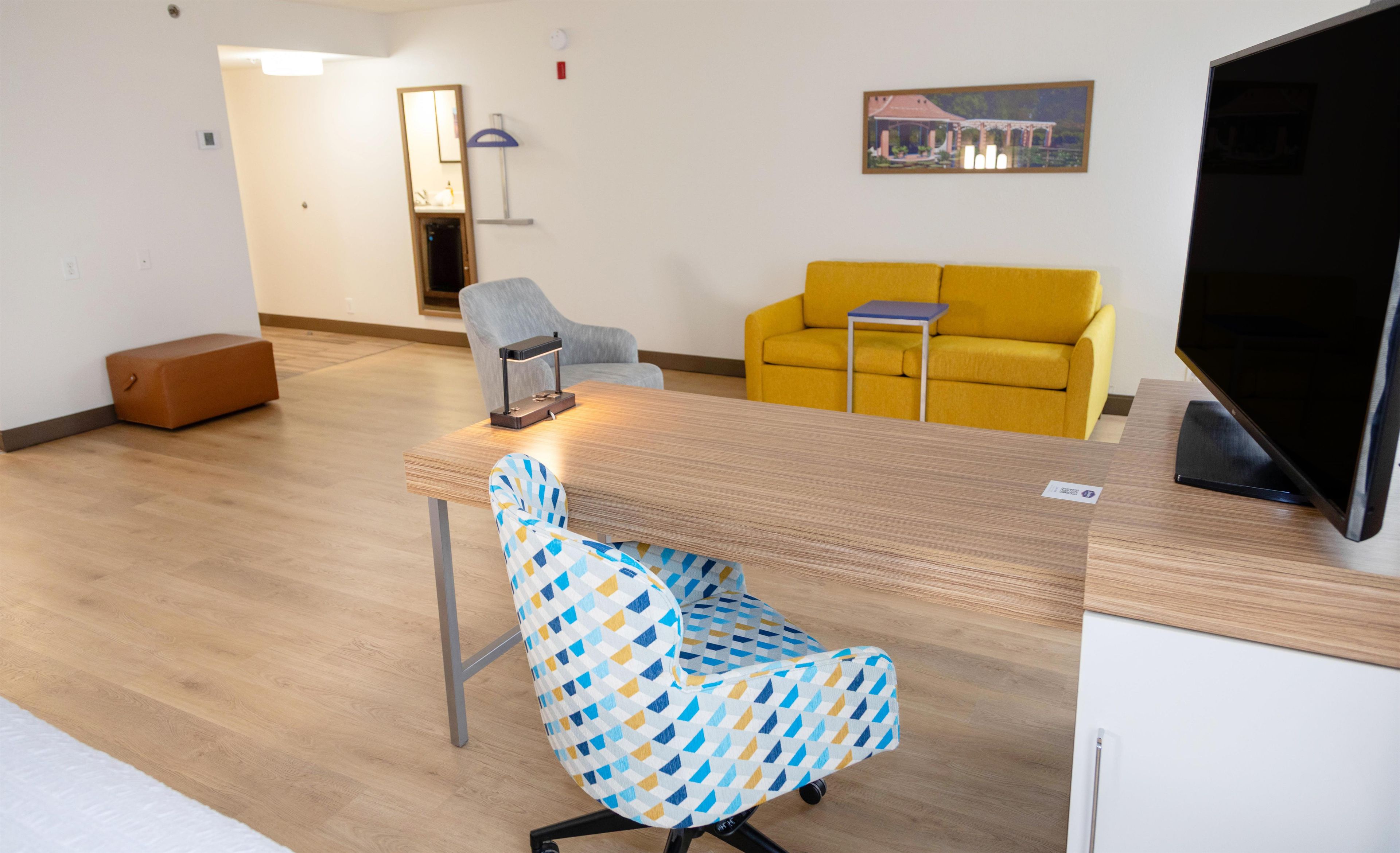 A modern living room with a wooden table, a patterned armchair, a yellow sofa, and a flat-screen TV.