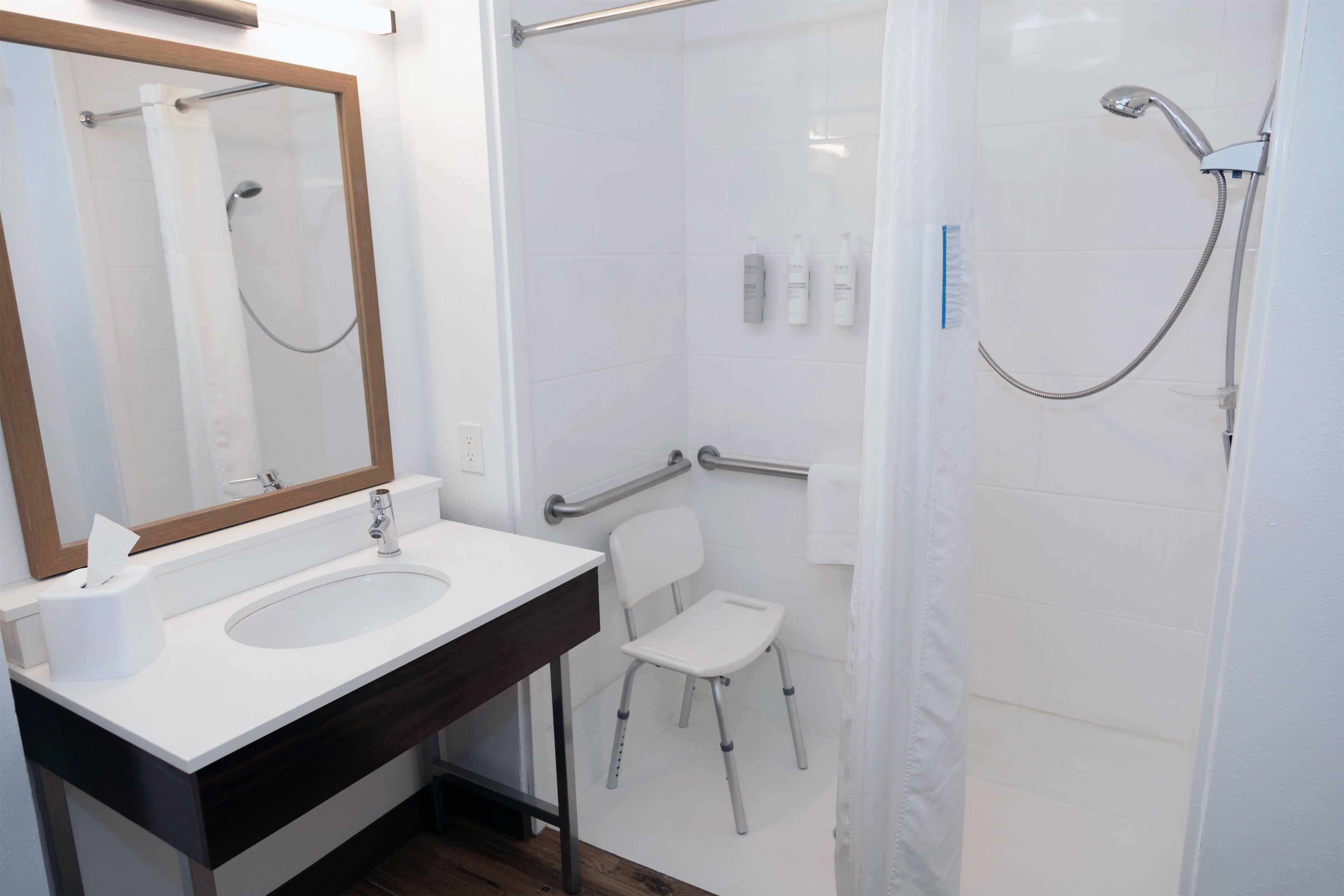 Une salle de bain avec un lavabo, un miroir, une douche et une chaise.