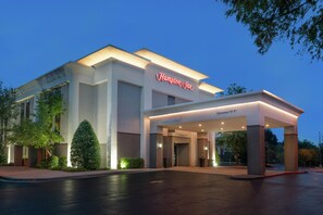 Et Hampton Inn hotel med en moderne facade, tydelig indgang og godt oplyst bygning.