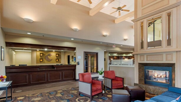 A hotel lobby with a reception desk, seating area, fireplace, and a ceiling fan.