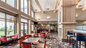 A spacious indoor area with multiple tables and chairs, large windows, and ceiling fans.