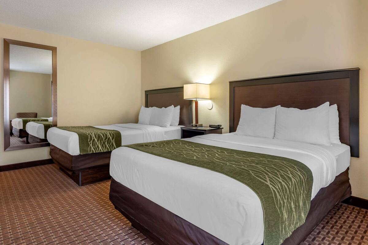 A hotel room with two beds, a large mirror, a nightstand, and a lamp.
