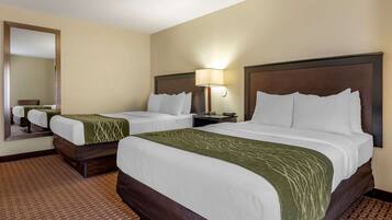 A hotel room with two beds, a large mirror, a nightstand, and a lamp.