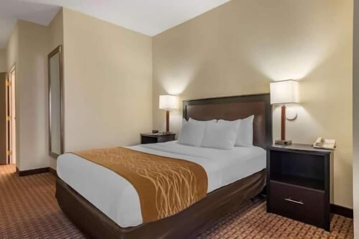 A hotel room with a bed, two bedside tables, a nightstand, and a lamp.