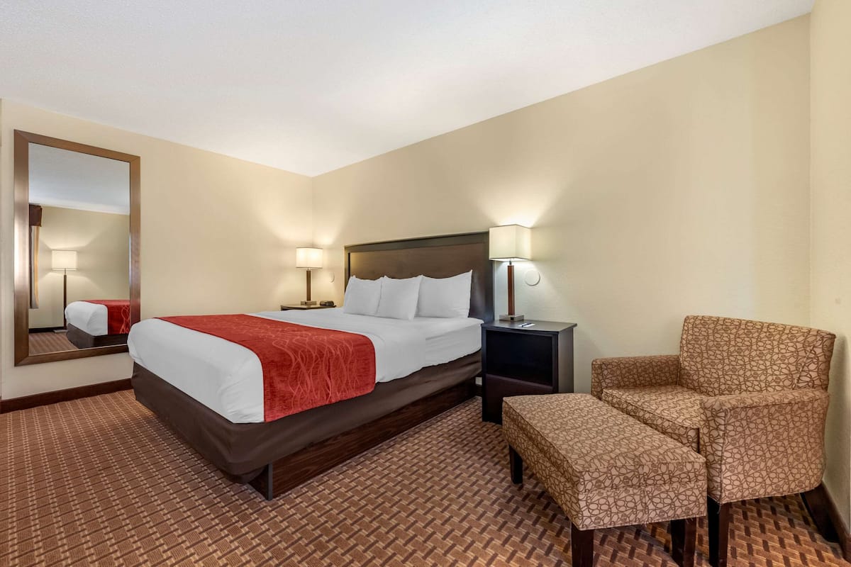 A hotel room with a bed, a chair, a nightstand, and a mirror.