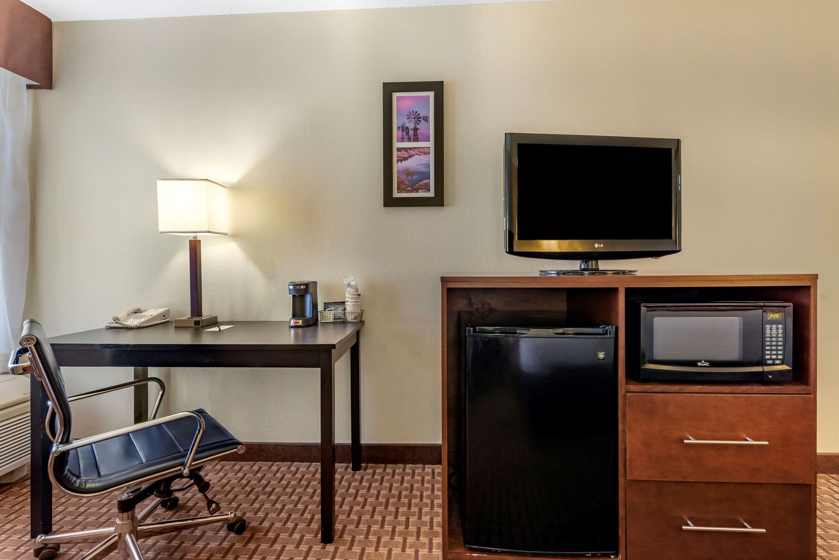 Une chambre d’hôtel équipée d’un bureau, d’une chaise, d’une télévision, d’un réfrigérateur, d’un four à micro-ondes et d’un tableau encadré au mur.