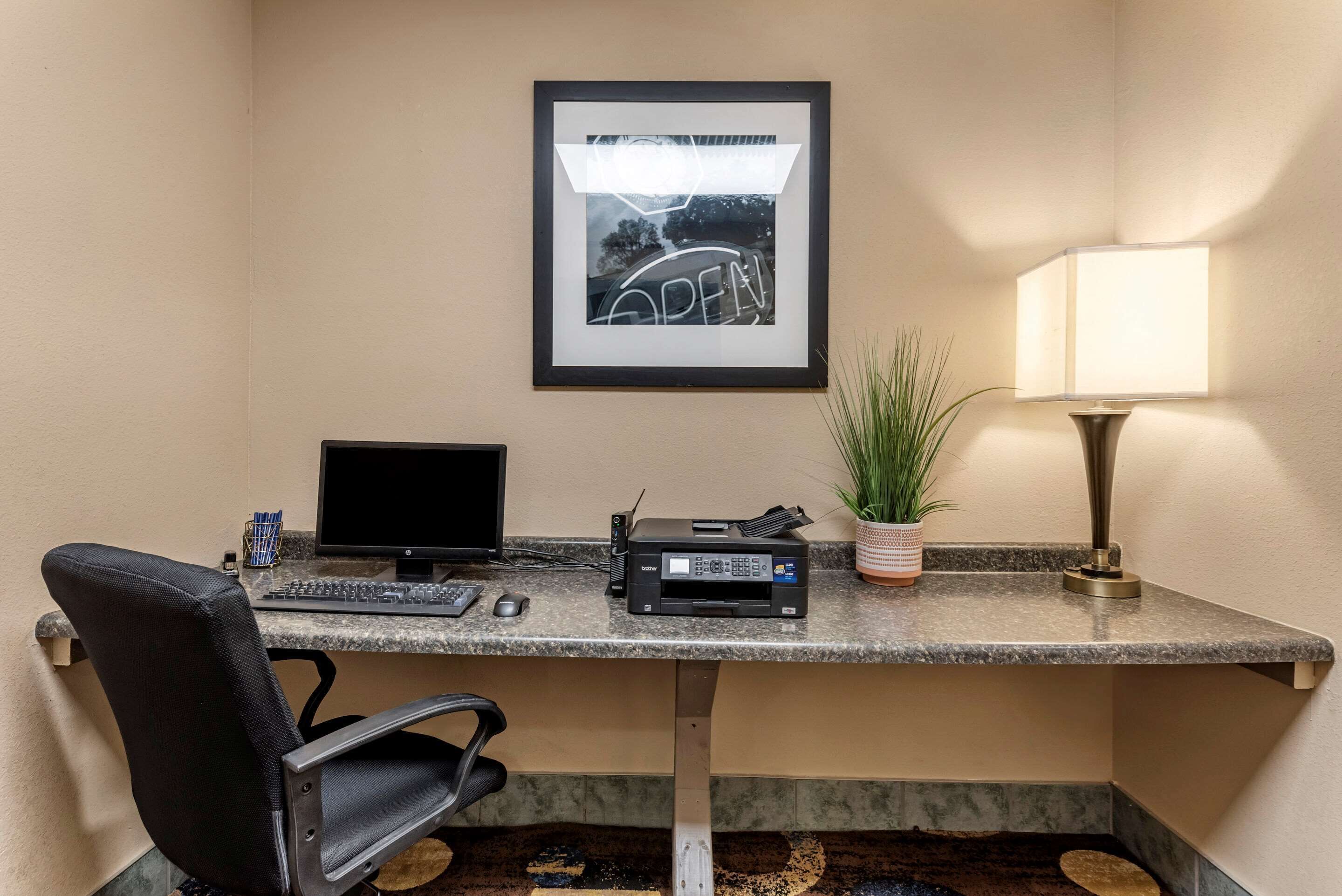 A hotel office with a desk, computer, printer, and a framed picture on the wall.