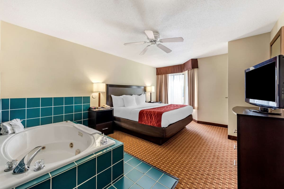 A hotel room with a large bed, a separate bathroom with a bathtub, a flat-screen TV, and a ceiling fan.