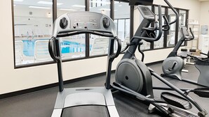 A gym with exercise equipment, a pool visible through the windows, and a water dispenser.