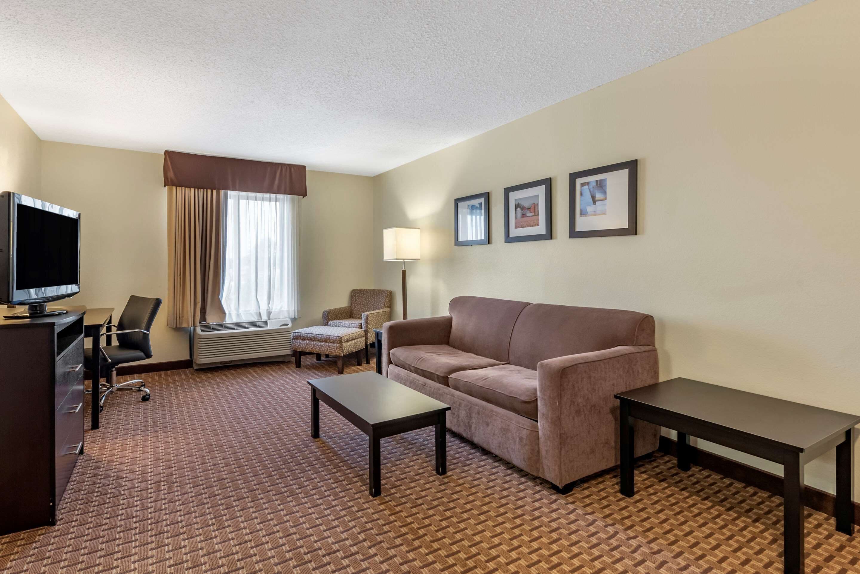 A hotel room with a sofa, two armchairs, a TV, a desk, and a lamp.