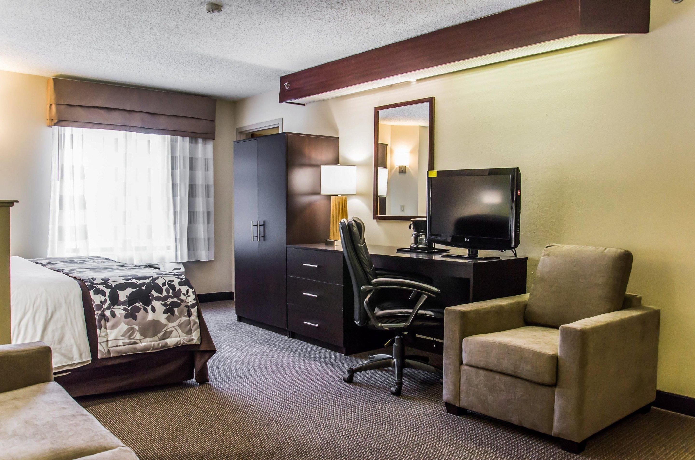 A hotel room with a bed, a desk with a computer, a chair, a sofa, a wardrobe, and a large mirror.
