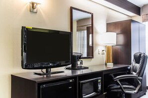 A hotel room with a flat-screen TV, a coffee maker, a microwave, a desk with a lamp, and a leather chair. - Sleep Inn Airport - Billy Graham Parkway (Charlotte)