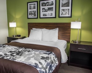 A hotel room with a bed, two bedside tables, a nightstand, a headboard, and three framed pictures on the wall. - Sleep Inn Historic Williamsburg (Williamsburg)