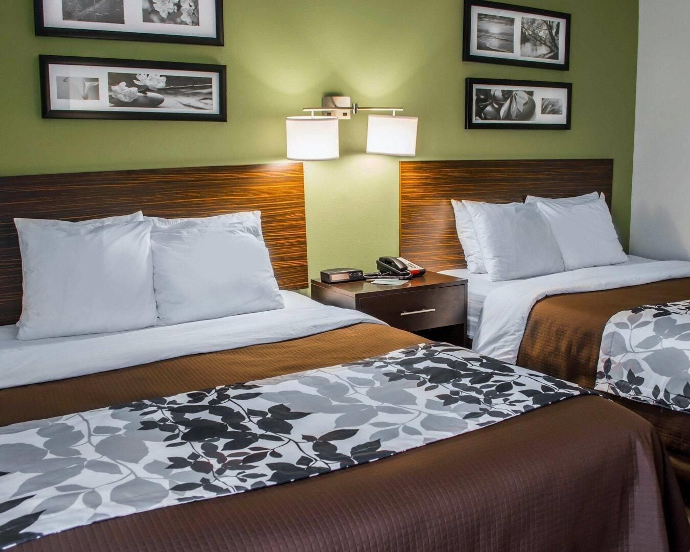 Habitación de hotel con dos camas, una mesita de noche, una lámpara y cuadros en la pared.