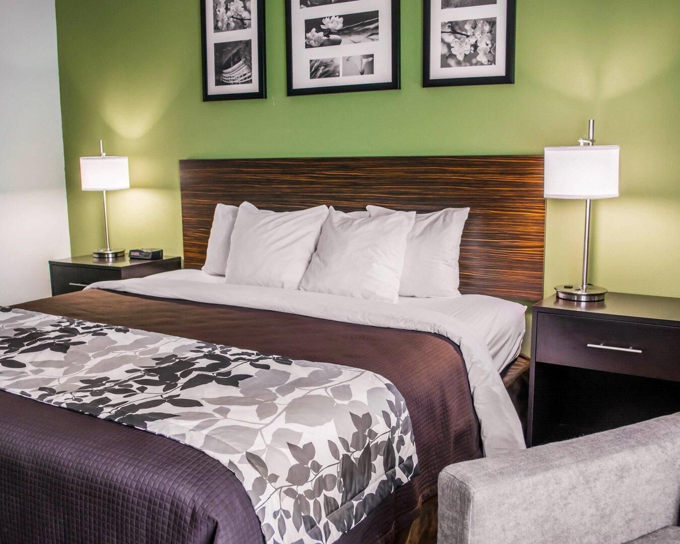 A hotel room with a bed, two bedside tables, a nightstand, a lamp, and a wall with framed pictures.