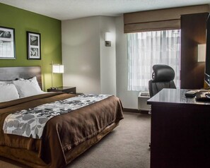 Quarto de hotel com uma cama, uma escrivaninha, uma cadeira, uma janela com cortinas e um painel com quadros.