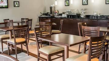 Un restaurante con mesas y sillas de madera, una zona de cocina y cuadros en las paredes.