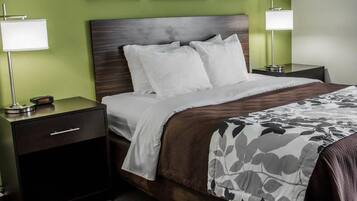 A neatly made bed with white linens and a floral-patterned throw, flanked by two bedside tables with lamps, in a room with green walls and framed pictures above the bed.