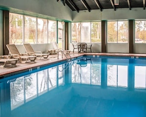 An indoor swimming pool with clear glass walls, lounge chairs, and a table. - Sleep Inn Historic Williamsburg (Williamsburg)