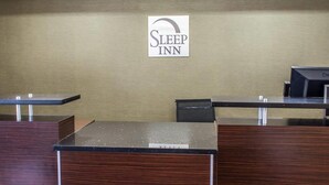 Sleep Inn -hotellin vastaanottotiski, jonka yläpuolella on kyltti, musta työpöytä ja puinen palvelutiski.