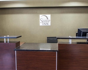 A Sleep Inn reception desk with a sign above it, a black desk, and a wooden counter. - Sleep Inn Historic Williamsburg (Williamsburg)