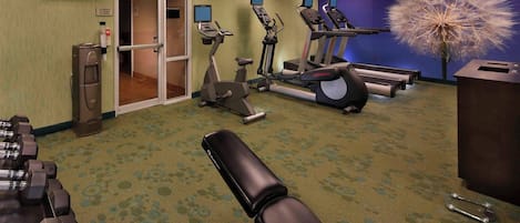 A hotel fitness room with exercise equipment, a water dispenser, and a television.