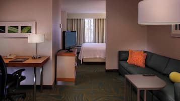 A hotel room with a desk, chair, bed, sofa, and a small table.