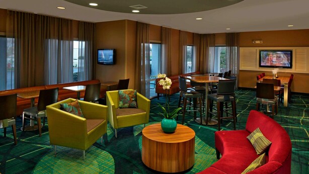 A hotel lobby with yellow armchairs, a red sofa, a wooden coffee table, a TV, and a dining area. - Springhill Suites by Marriott Mystic Waterford (Quaker Hill)