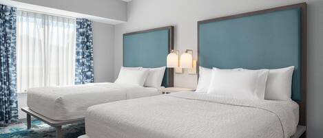 Habitación de hotel con dos camas, una mesita de noche, una lámpara y una ventana con cortinas.