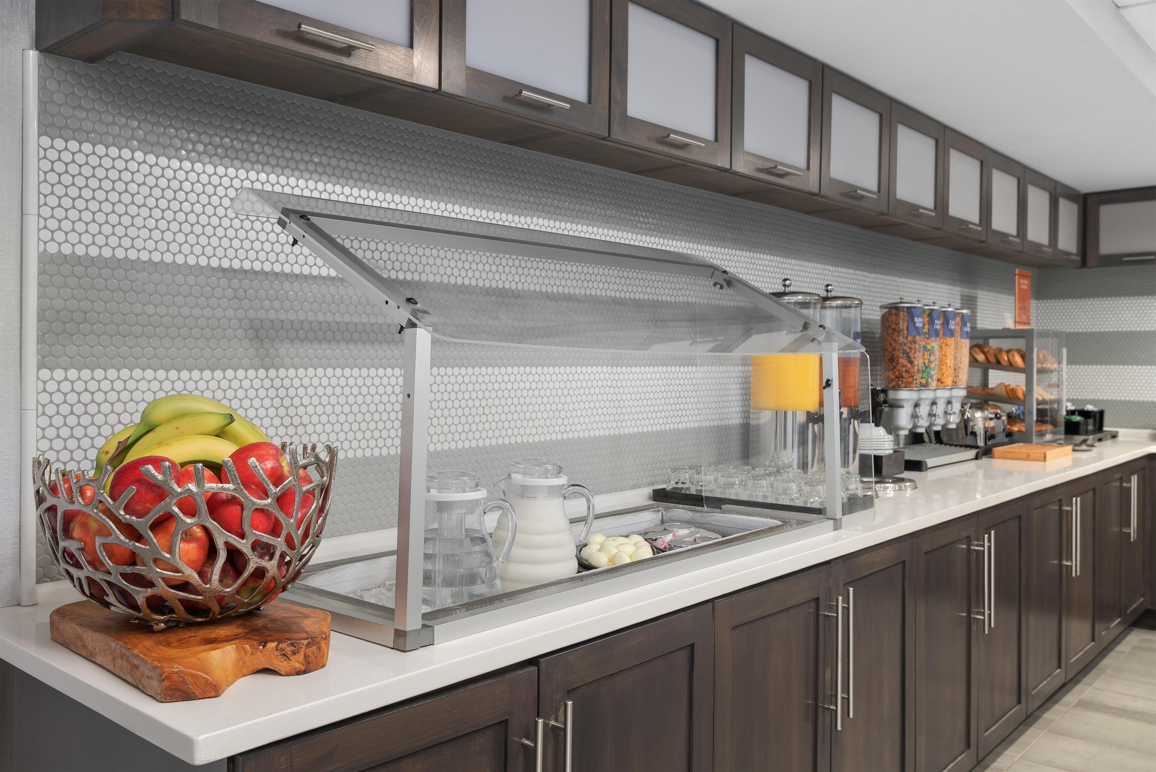 A modern kitchen with a breakfast bar, a fruit bowl, and a beverage station.