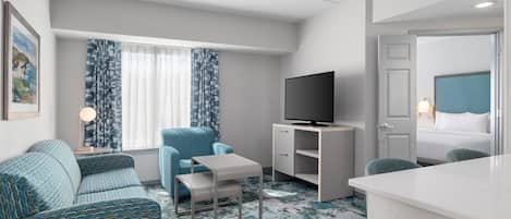 A modern hotel room with a sofa, a small table, a TV, and a bed.