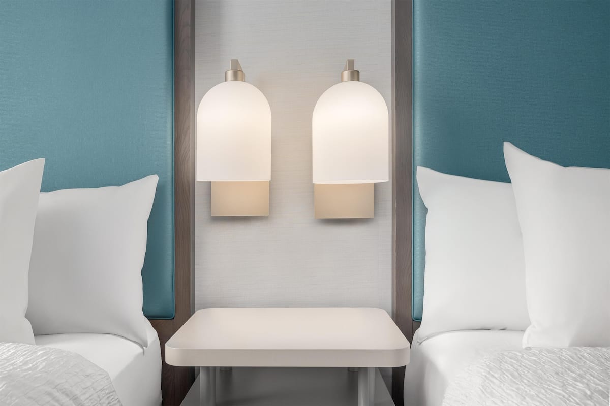 Una camera d'albergo con due letti, un tavolino e lampade a parete.