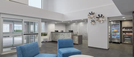A modern hotel lobby with seating, a reception desk, and a minibar.