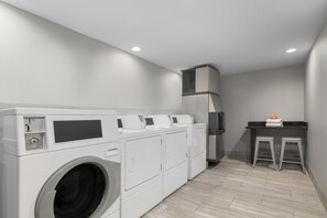 A laundry room with a front-loading washer and dryer, a small countertop with a towel dispenser, and a vented range hood above the stove. - Homewood Suites by Hilton Williamsburg (Williamsburg)