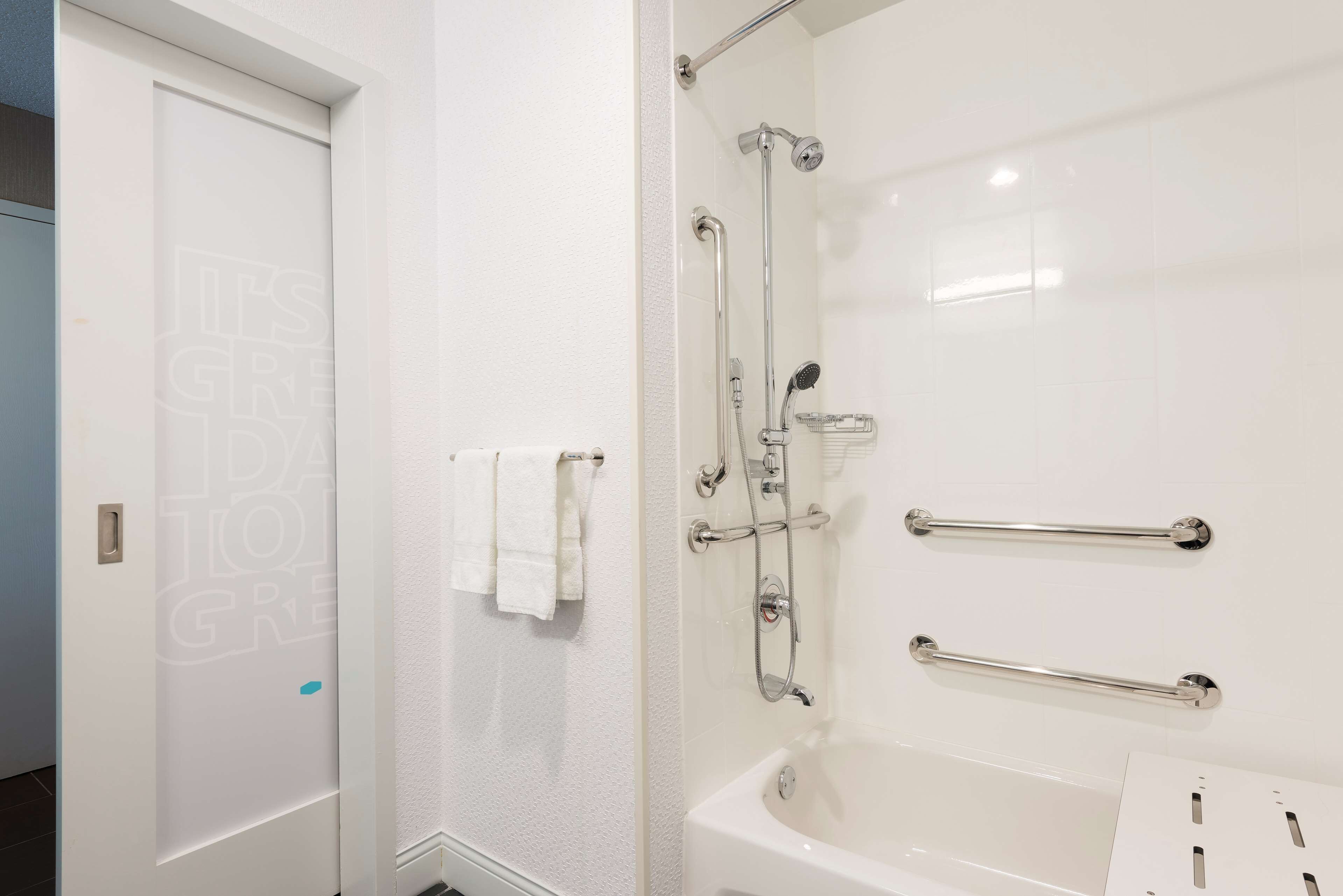 Un baño con bañera, ducha con barras de apoyo y un perchero para toallas.