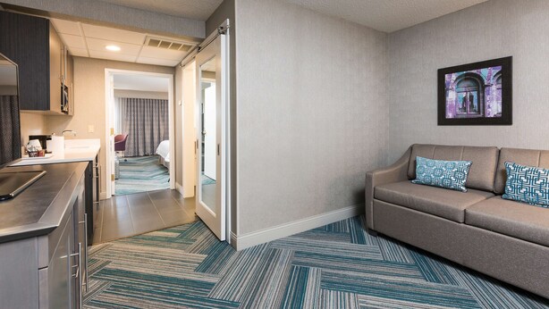 A hotel room with a kitchenette, a sofa with patterned cushions, a framed picture on the wall, and a patterned carpet. - Hampton Inn Midland (Midland)