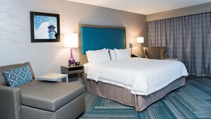 A hotel room with a large bed, a sofa, a nightstand, a lamp, and a framed picture on the wall. - Hampton Inn Midland (Midland)