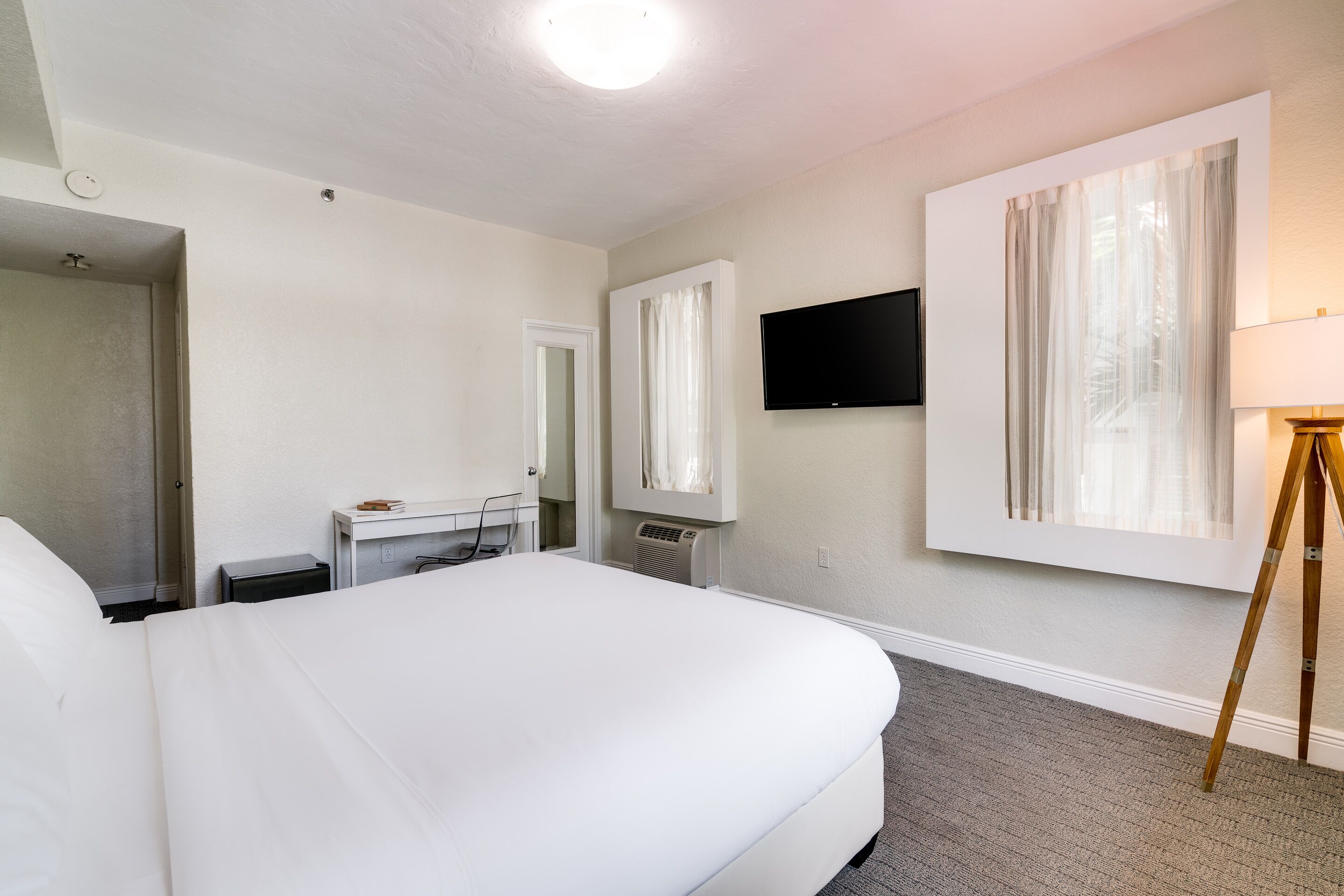 Habitació d'hotel amb un llit gran, escriptori amb cadira, televisió plana penjada a la paret i finestra amb cortines transparents.