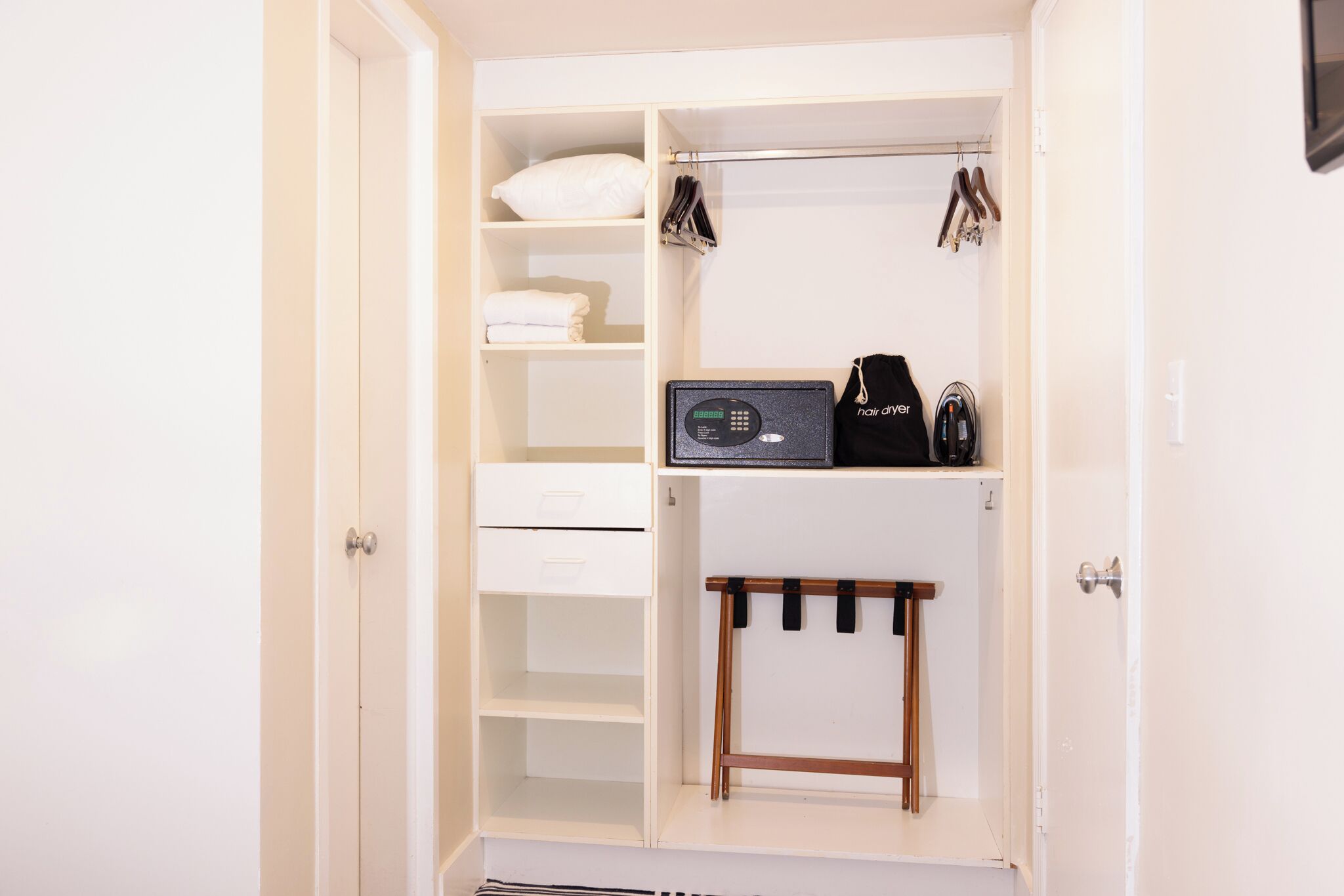 Un armario blanco con estantes, barra para colgar ropa y un pequeño taburete de madera.