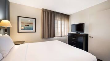 Habitación de hotel con una cama grande, un televisor en una cómoda, un cuadro en la pared y una ventana con cortinas.